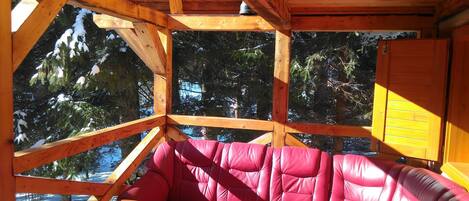 A wooden cabin interior with a red leather sofa, wooden beams, and a view of snow-covered trees.