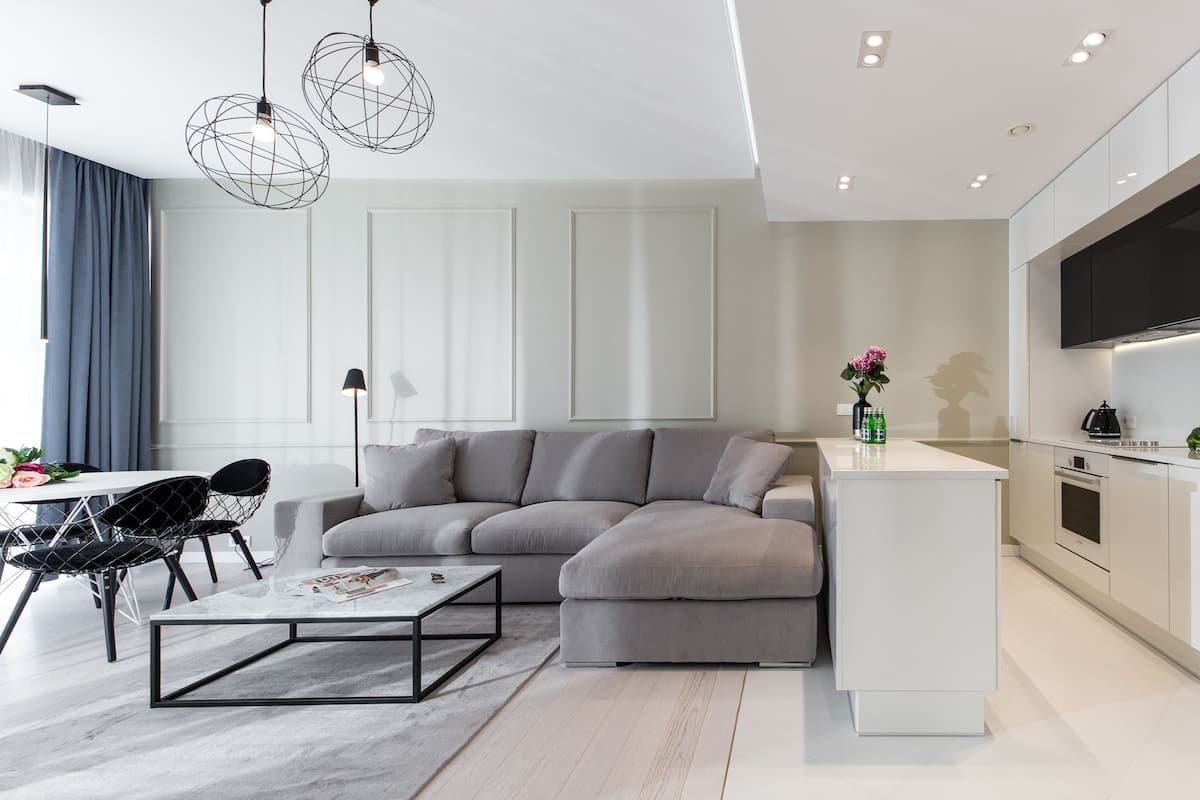 A modern living room with a grey sectional sofa, a coffee table, and a dining area with chairs.