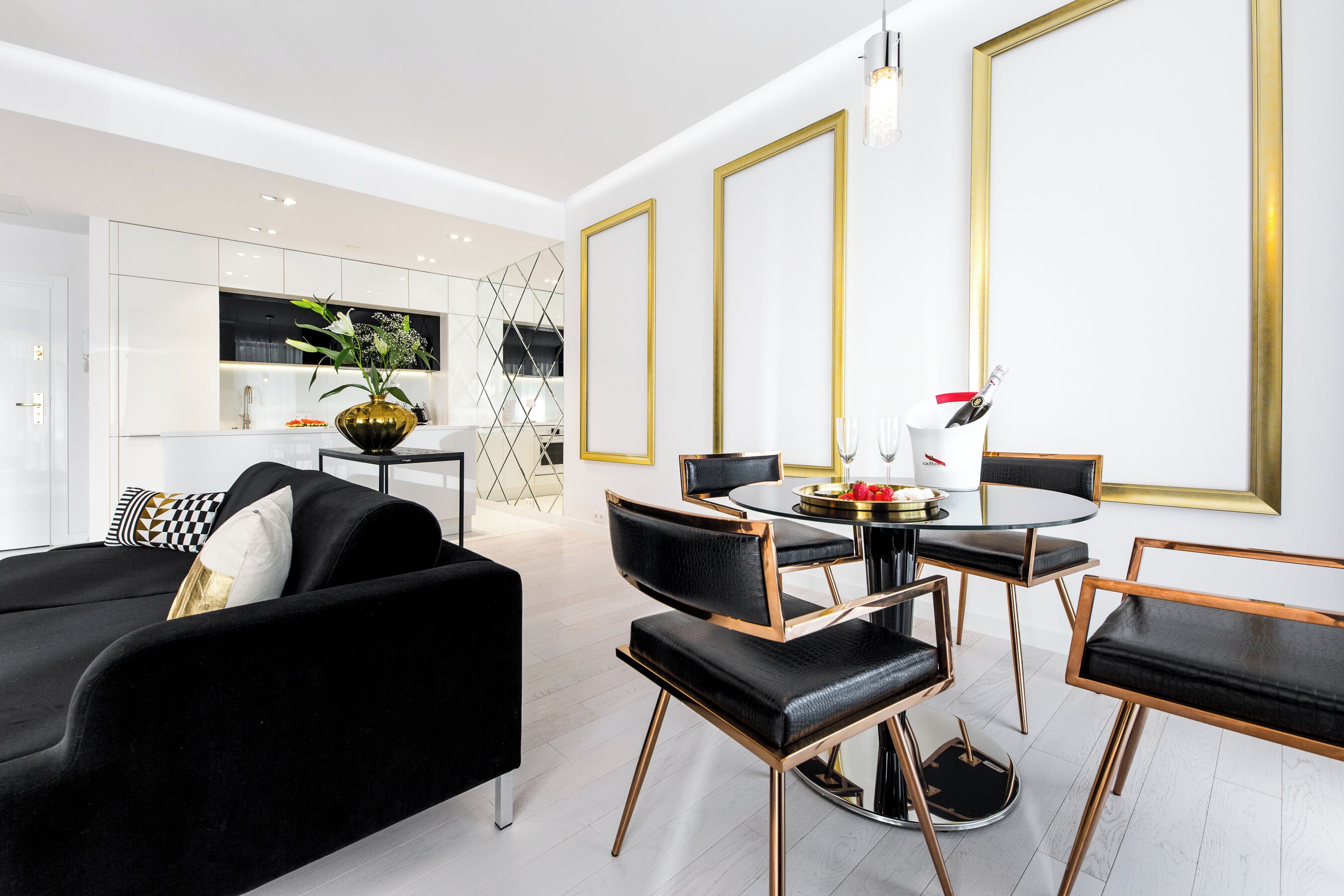 Una sala moderna con un sofá negro, una mesa de comedor con sillas y una cocina al fondo.