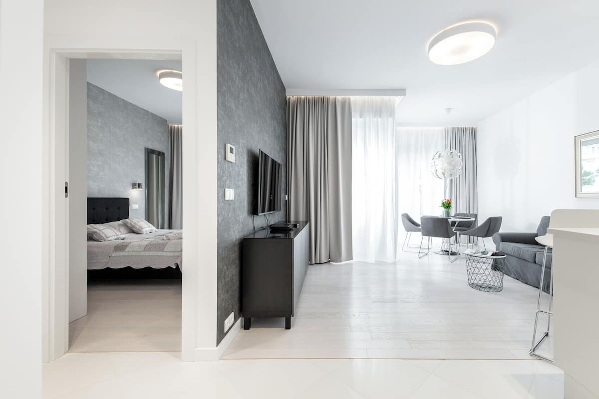 A modern hotel room with a bed, a TV, a desk, and a dining area.