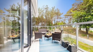 A modern outdoor seating area with wicker furniture, a glass balustrade, and potted plants. - DUNE B - FAF (Mielno)