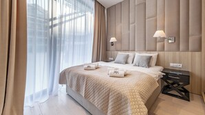 A modern bedroom with a large bed, a bedside table with a lamp, and a view through sheer curtains. - DUNE B - FAF (Mielno)