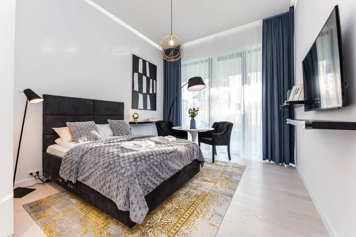 A modern bedroom with a large bed, a bedside table, a TV, and a seating area with a chair and table.