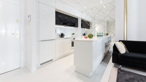 A modern kitchen with white cabinetry, a central island, and a black sofa in a living area. - DUNE B - FAF (Mielno)