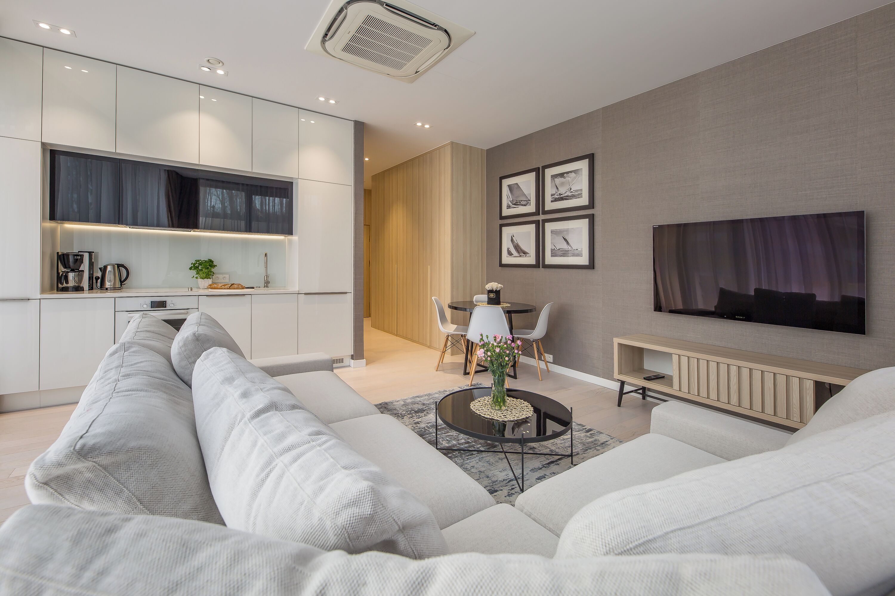 Una sala moderna con un sofá modular, una mesita de centro, un comedor con una mesa y sillas, y un televisor montado en la pared.