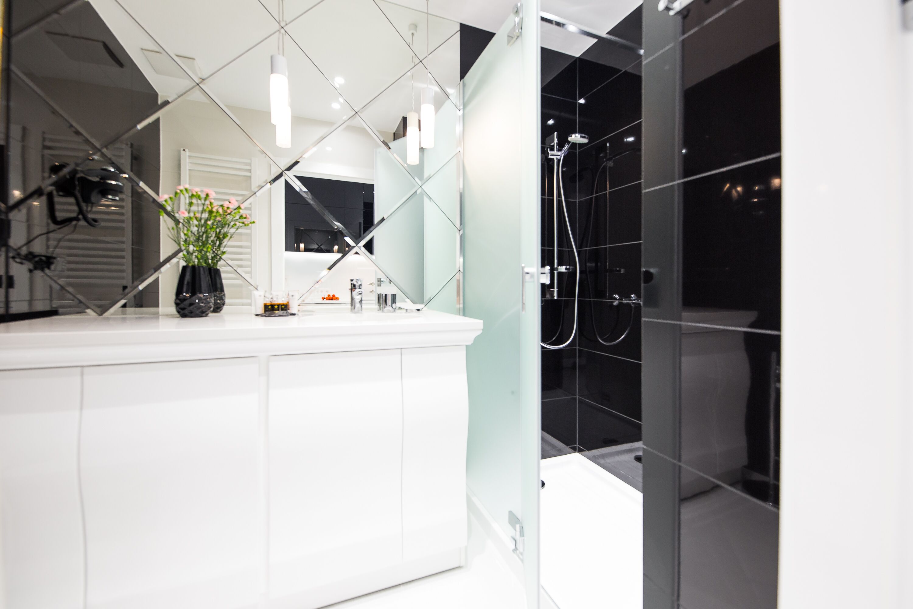 Un baño moderno con un tocador blanco, cabina de ducha de vidrio y un florero con flores en la encimera.
