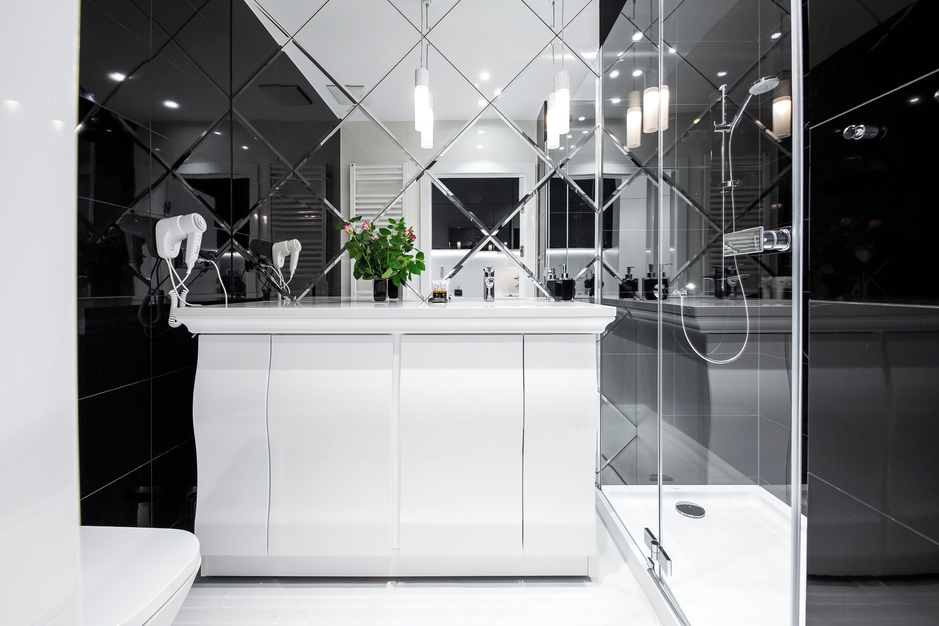 A modern bathroom with a white vanity, a glass shower enclosure, and a large mirror reflecting the room.