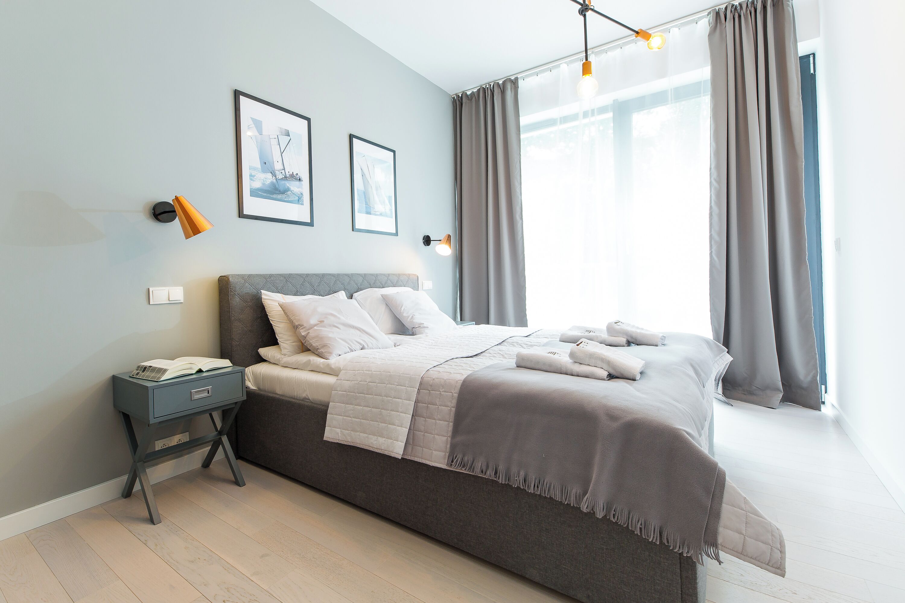 A modern bedroom with a bed, bedside table, and a window with curtains.