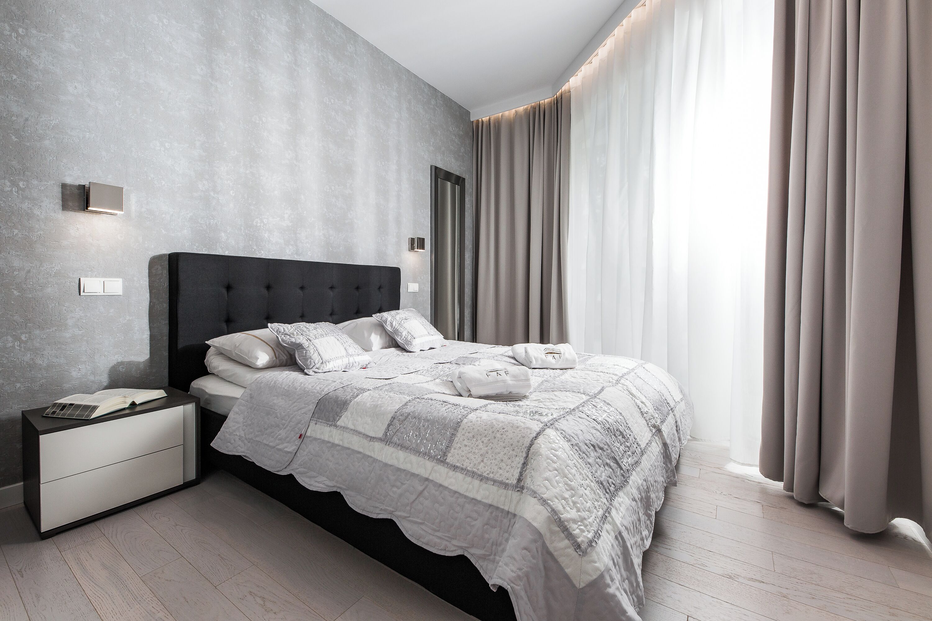 A modern bedroom with a large bed, a nightstand, and a wall-mounted light.
