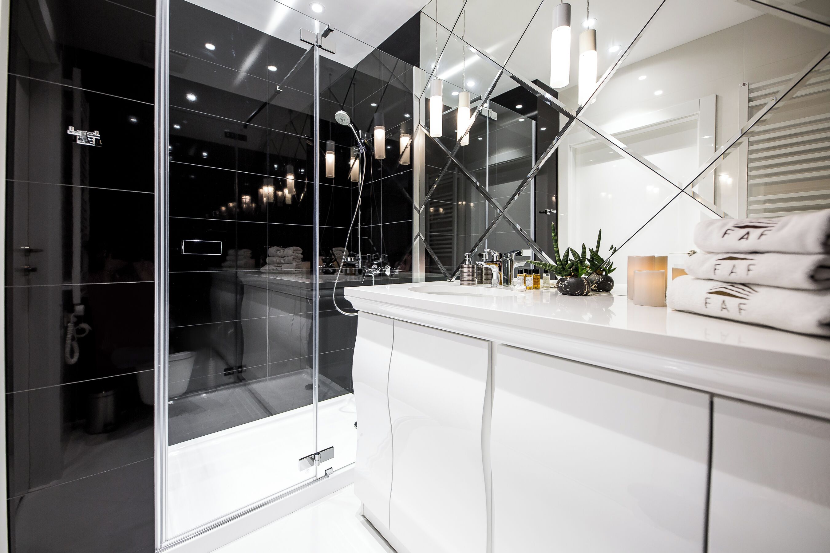 A modern bathroom with a glass shower enclosure, white cabinetry, and a vanity with towels.