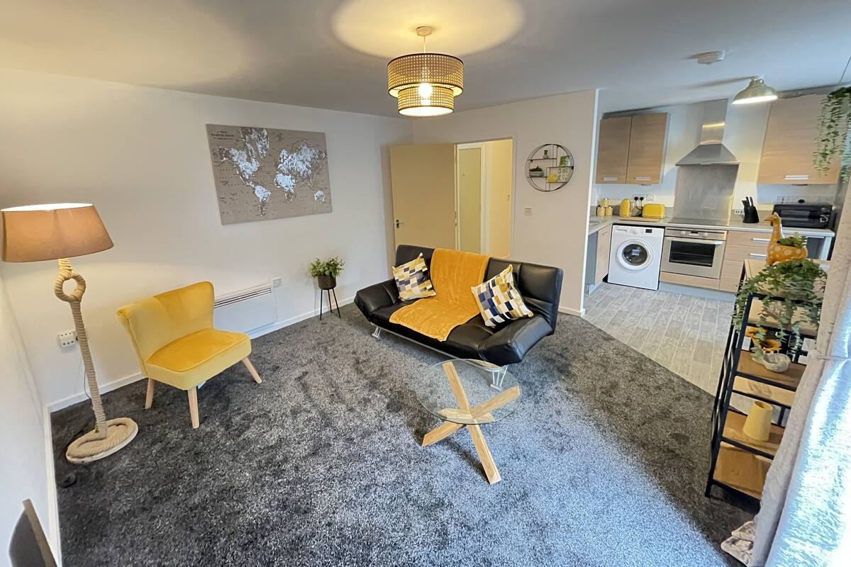 A compact living space with a sofa, a small table, a lamp, a radiator, a world map artwork, and a kitchenette.