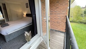 A bedroom with a bed, a nightstand, a lamp, and a window with curtains. - Grand Central Littleover Deluxe (Derby)