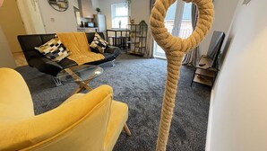 A living room with a sofa, a yellow armchair, a glass coffee table, and a large rope swing. - Grand Central Littleover Deluxe (Derby)