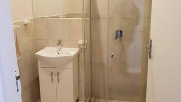 Een badkamer met een douchecabine van glas, een wastafel en een toilet.