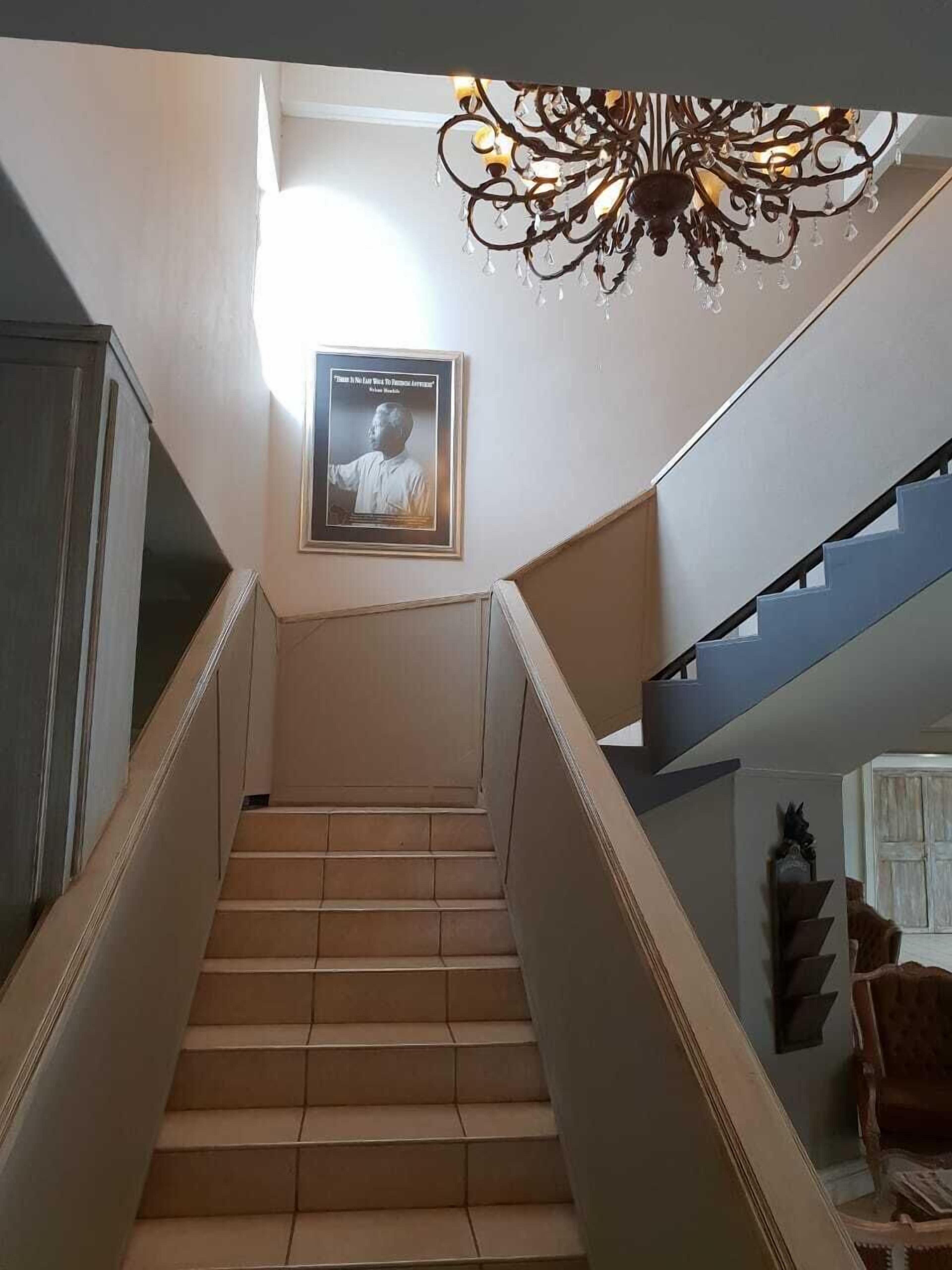 Una escalera con un candelabro, una cita enmarcada en la pared y una silla al fondo.