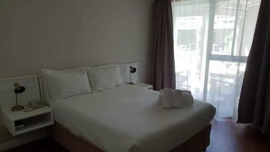A hotel room with a large bed, a bedside table with a lamp, and a view of the outdoors through a window. - Savoy hotel (Jeffreys Bay)