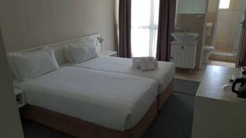 A hotel room with two beds, a bathroom, and a shower area.