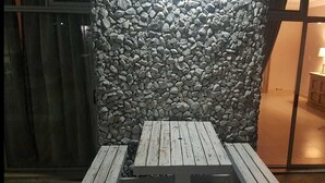A wooden table with a stone wall backdrop, a glass door leading to an interior room with a lamp and a mirror. - Savoy hotel (Jeffreys Bay)