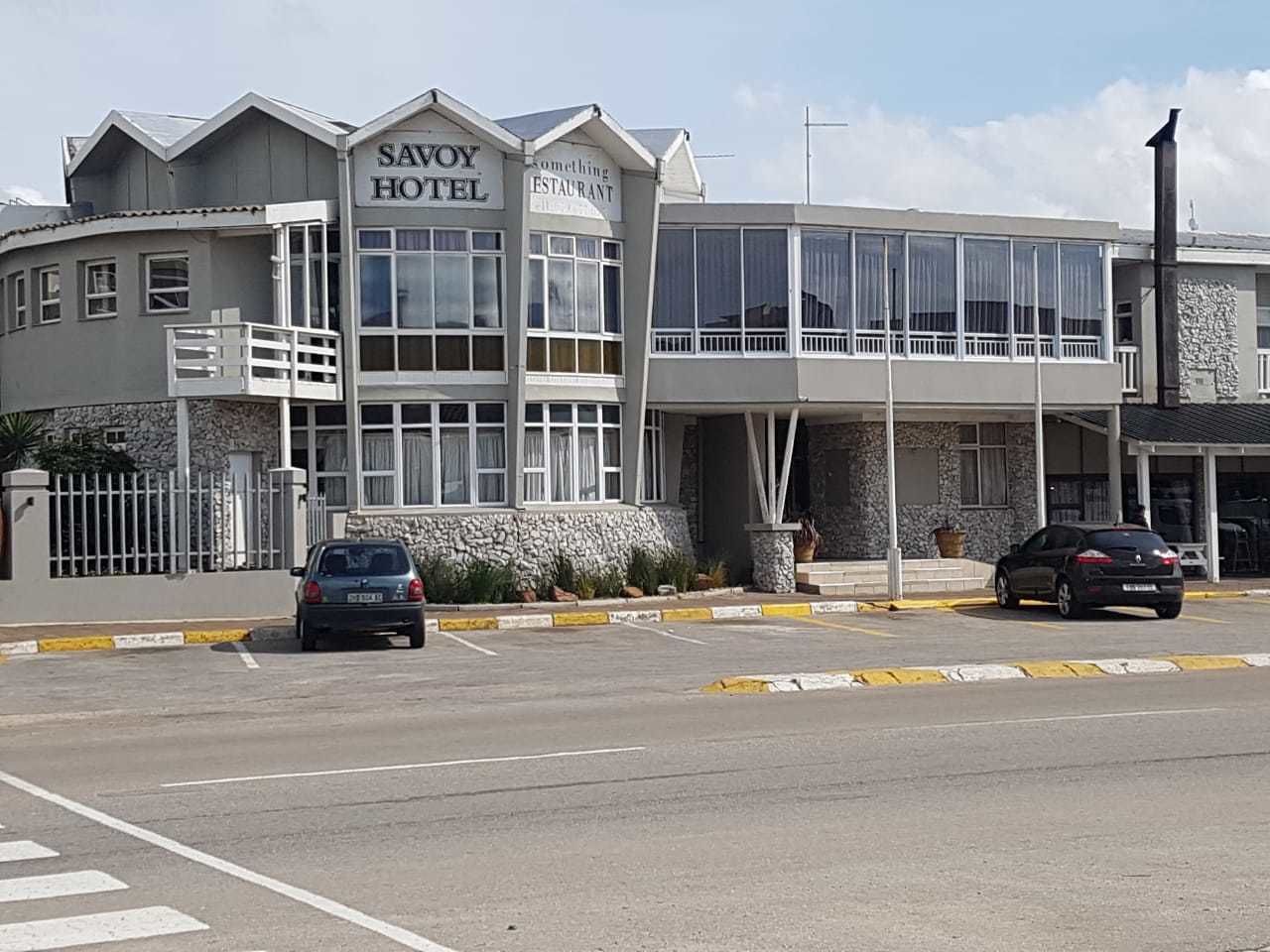 Un edificio de dos pisos con un cartel que dice 'SAVOY HOTEL' y 'Something Restaurant'.