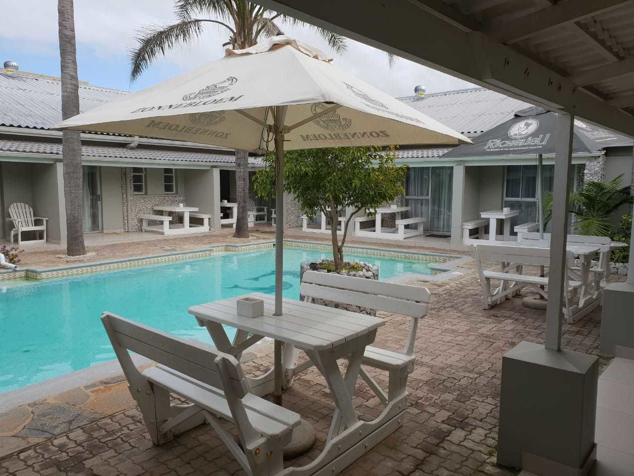 A poolside area with white furniture and umbrellas, surrounded by buildings with signage.