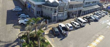 A hotel with a prominent corner building, a parking lot with several cars, and palm trees.