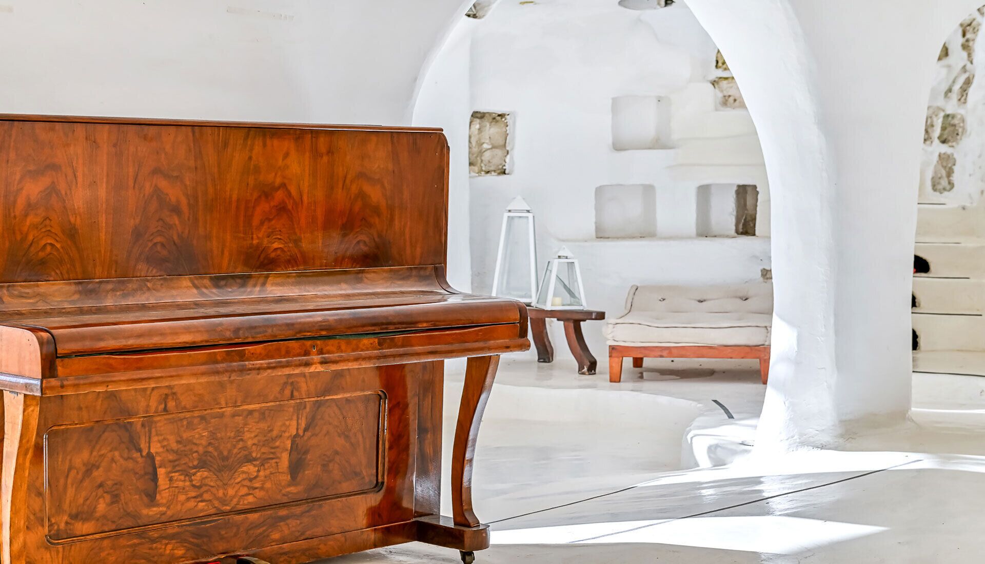 Un piano de madera en una habitación luminosa y blanca, con un sofá blanco y objetos decorativos.