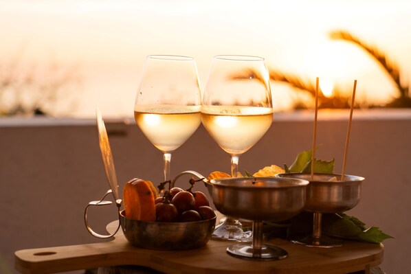 Two glasses of white wine, a metal bowl with fruits, and a metal bowl with leaves on a wooden table against a sunset background. - Ravino Secret Retreat (Forio)