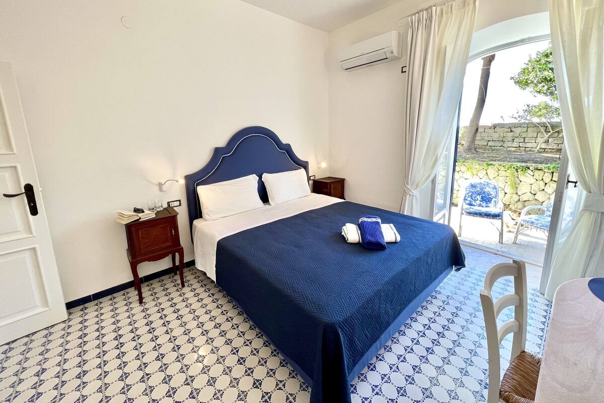 Habitación de hotel con cama, mesita de noche, aire acondicionado y vista al exterior.