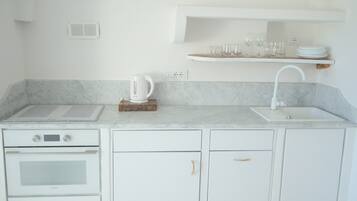 A kitchen with white cabinets, a built-in oven, a sink, and a shelf above the counter holding glasses and plates.