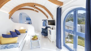 Un intérieur moderne avec un plafond incurvé, un canapé avec des coussins, une petite table avec une plante, un téléviseur et une fenêtre donnant sur un paysage verdoyant.