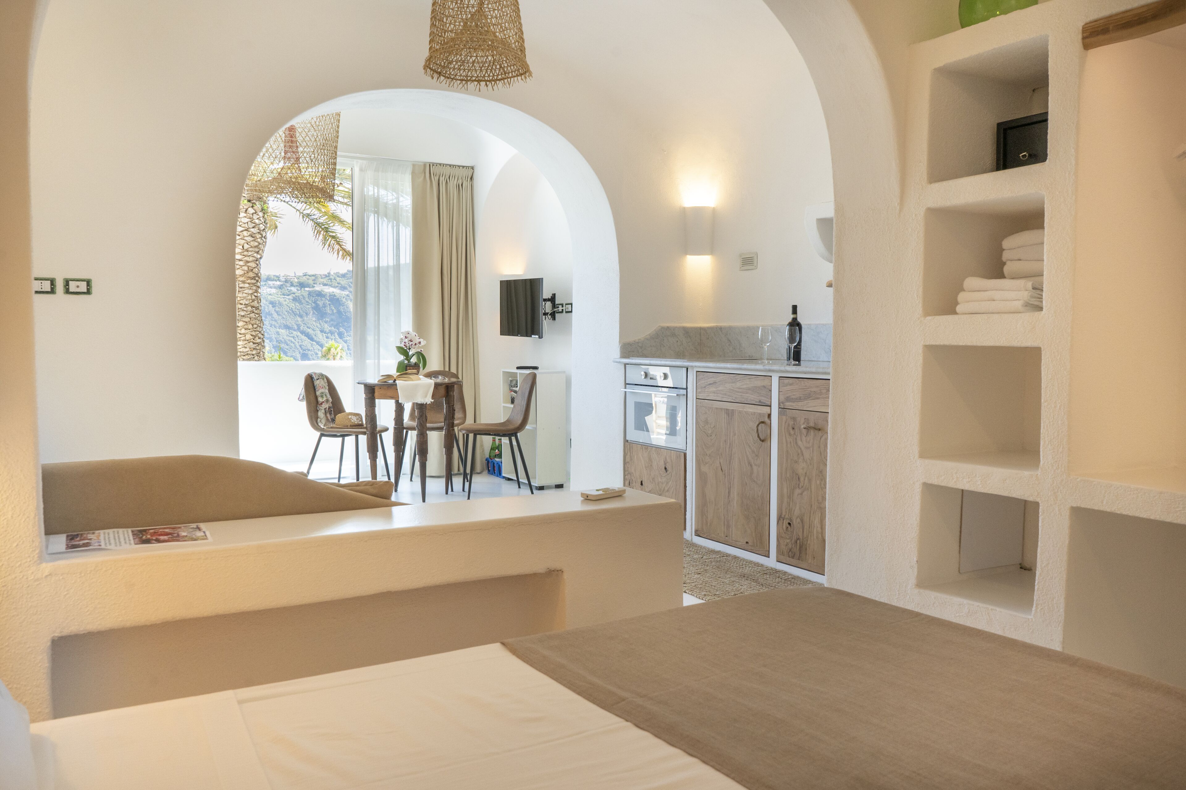 Una camera moderna con un'ampia finestra, un'area pranzo con sedie, una cucina con mobili in legno e uno scaffale integrato con asciugamani.