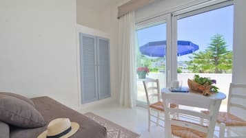 A room with a sofa, a dining table with chairs, a hat on the sofa, and a view of a balcony with an umbrella.