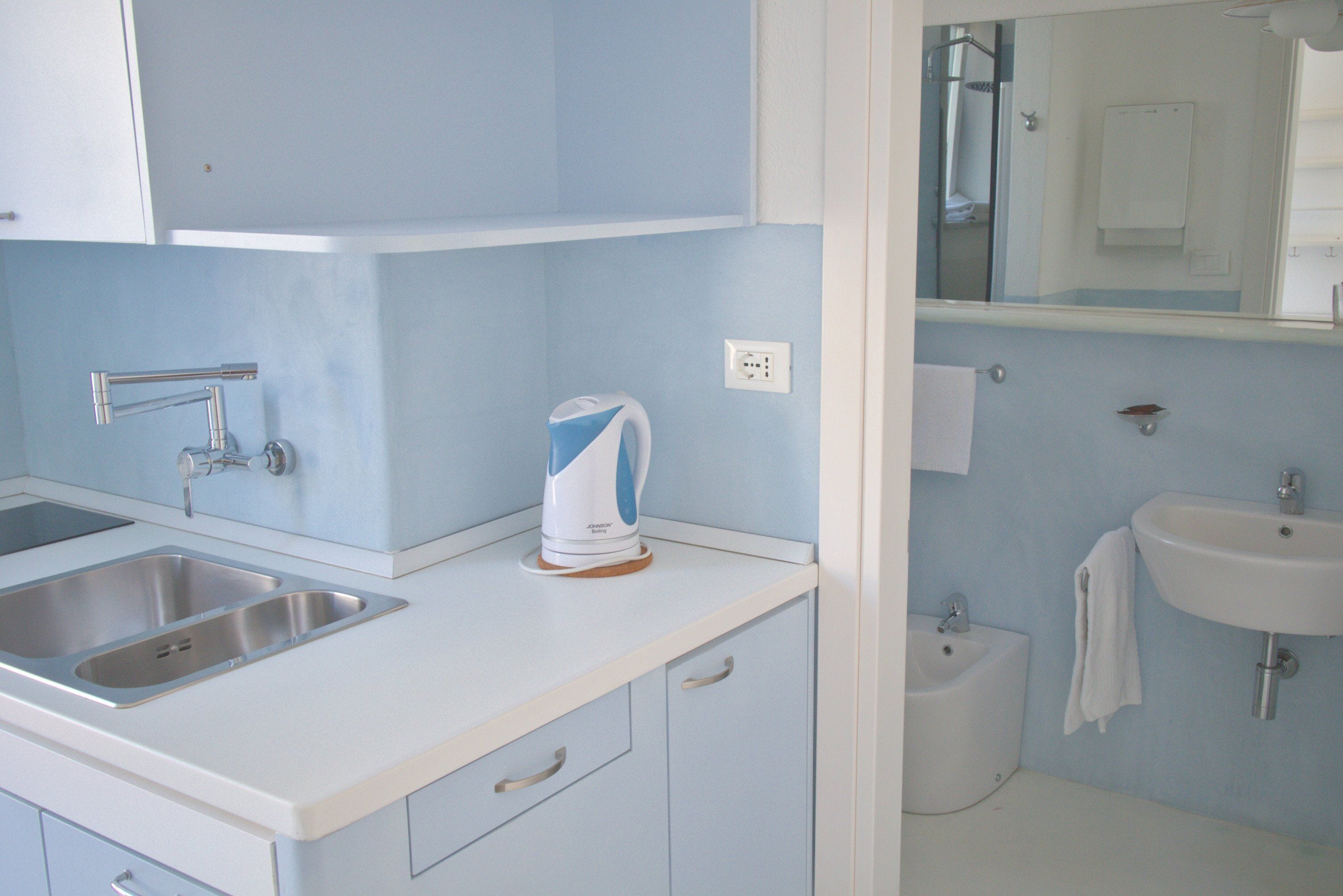 A kitchen with a double sink, a kettle, and a small cabinet.