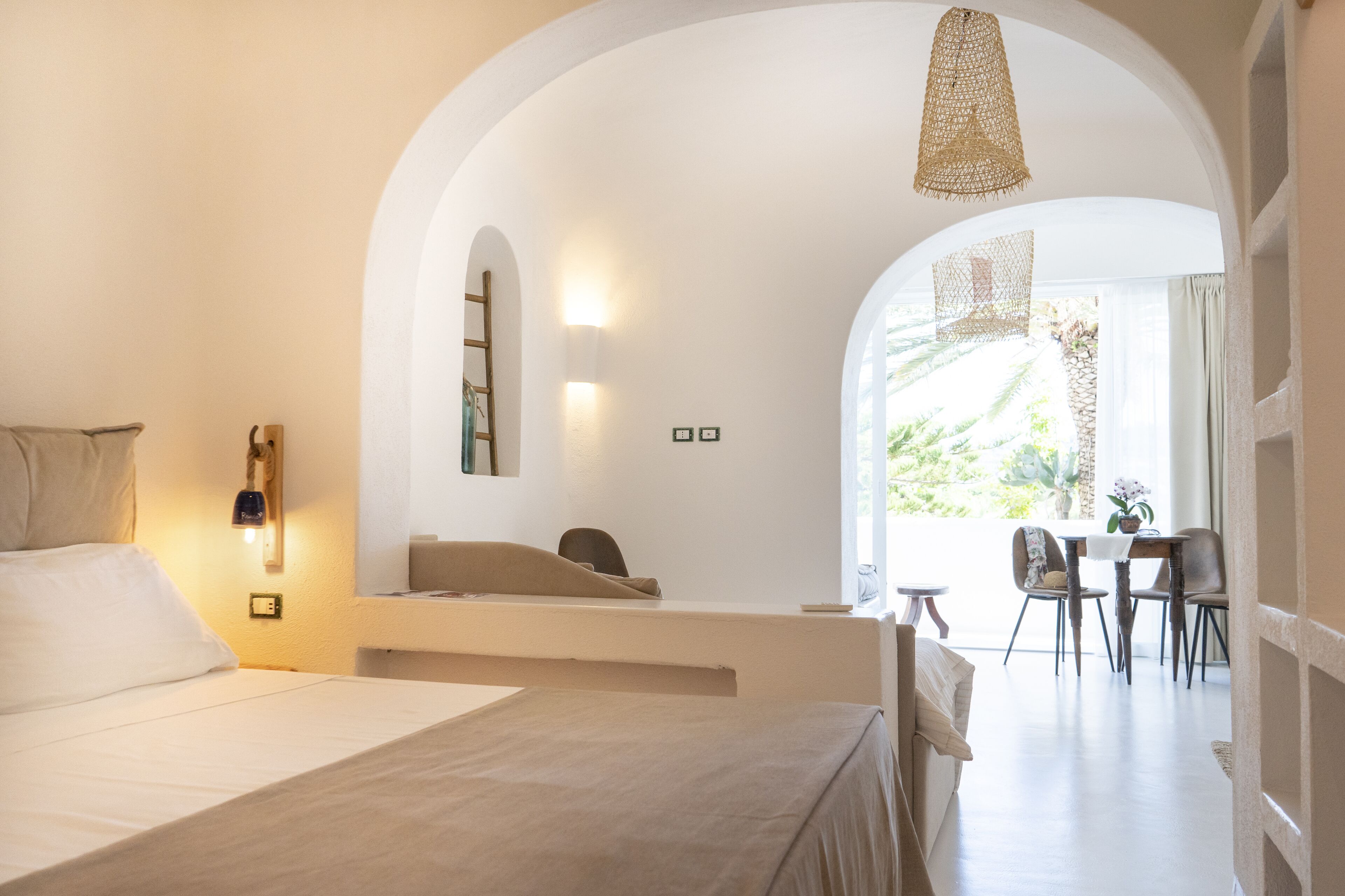 A bedroom with a bed, a desk, and a chair. There is a window with a view of greenery.