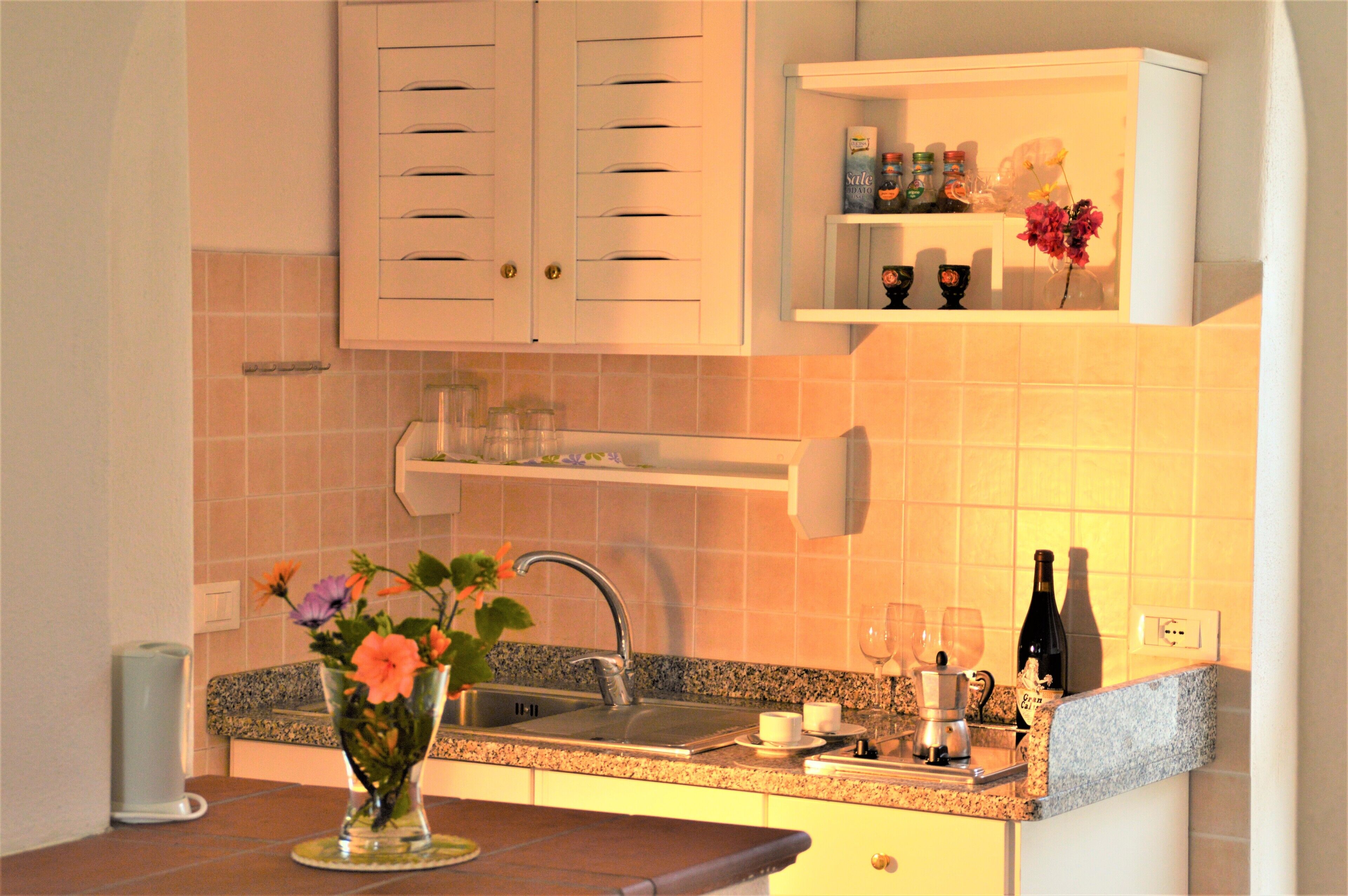 A kitchen with a granite countertop, a sink, and a shelf above the countertop.