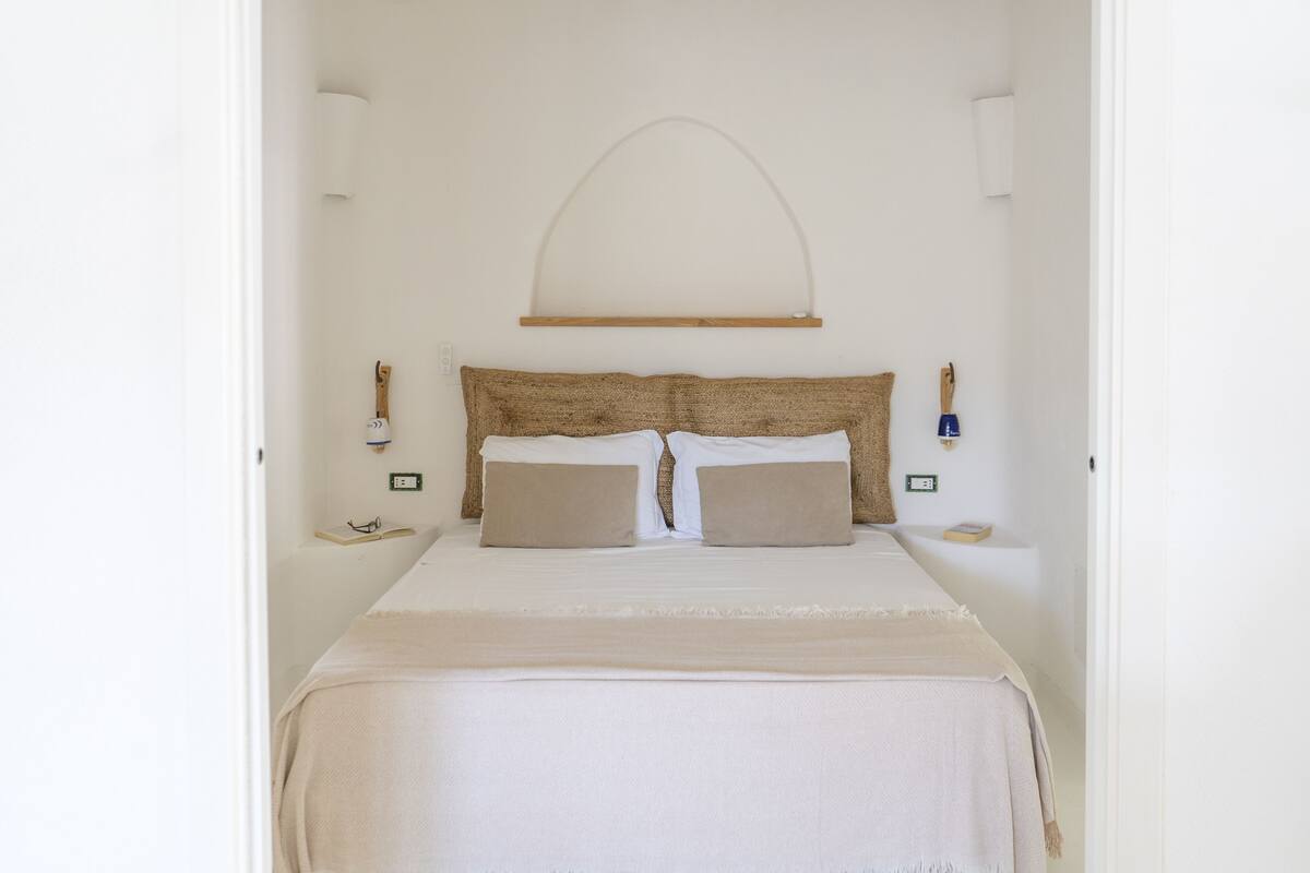 Un dormitorio con cama, dos mesitas de noche, una lámpara de pared y un cabecero de madera.