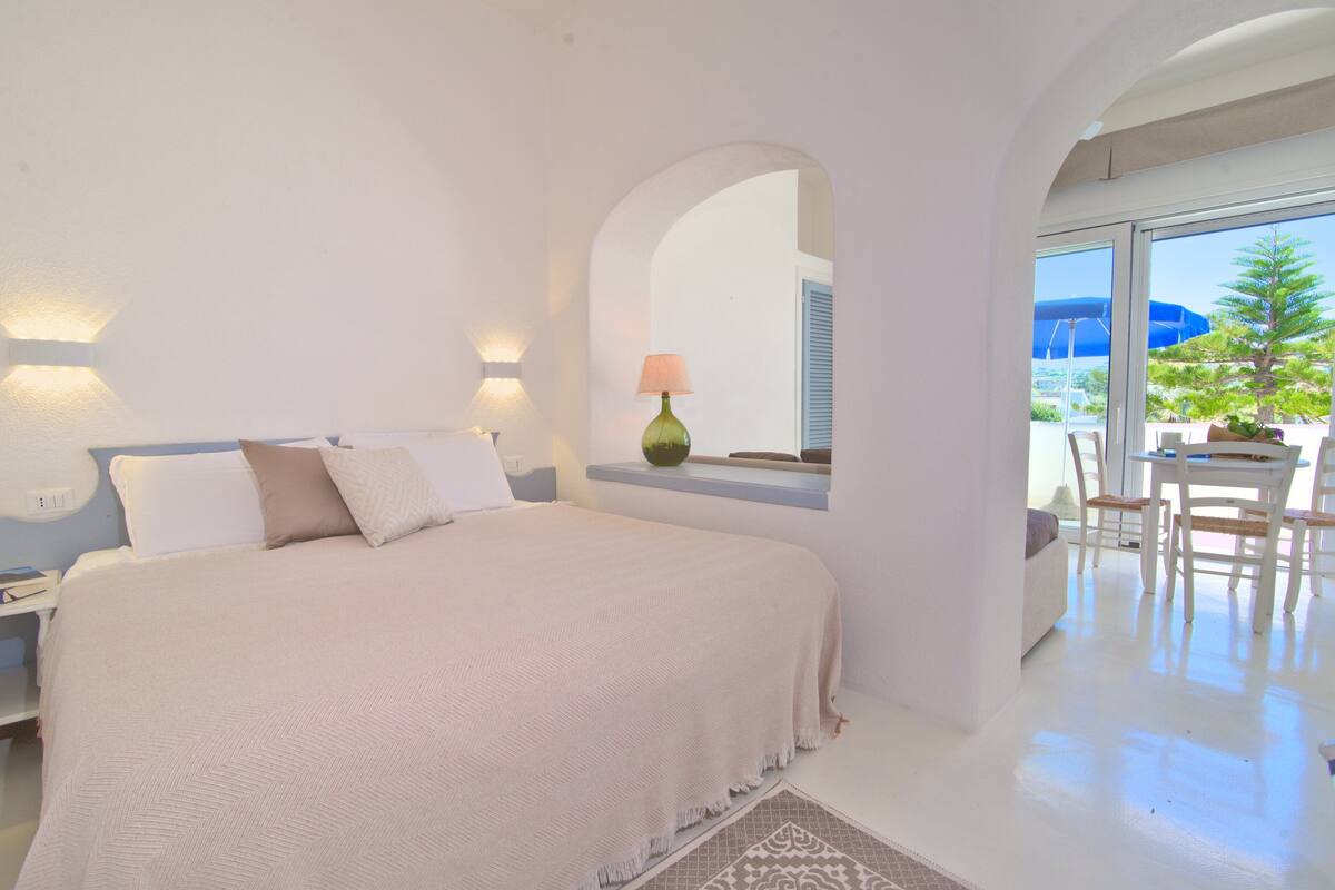 Un dormitorio con una cama grande, una mesita de noche, una lámpara y vistas al exterior.