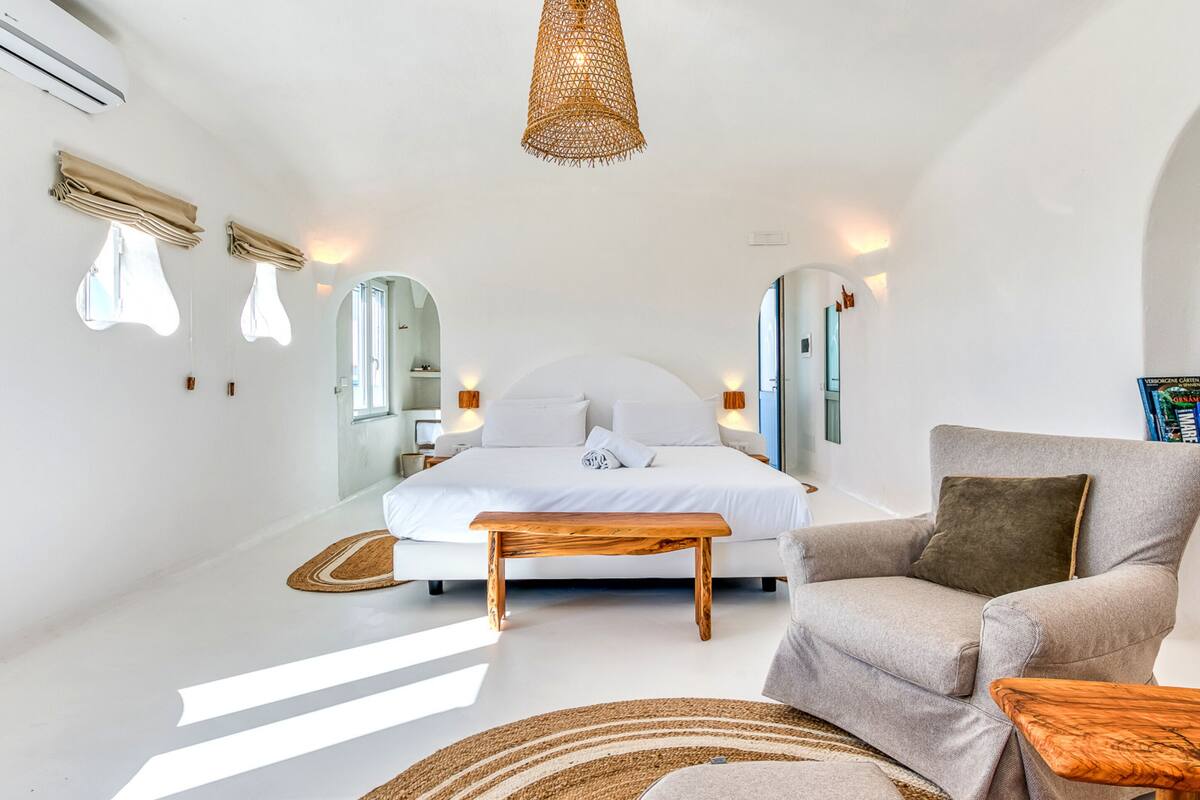 Un dormitorio moderno con una cama grande, un sofá, un banco de madera y una lámpara colgante.
