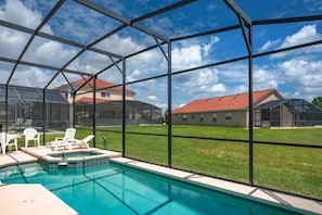 A swimming pool with a glass enclosure, surrounded by lawn chairs and a view of houses.