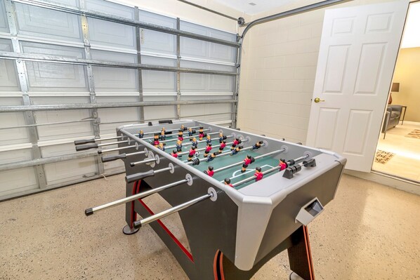 A foosball table in a room with a garage door and a white door.