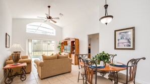A spacious living room with a high ceiling, a dining area with a wooden table and chairs, and a large window providing natural light. - Aviana - Pet Friendly 4bd/3ba Pool Home - #4av242 (Davenport)