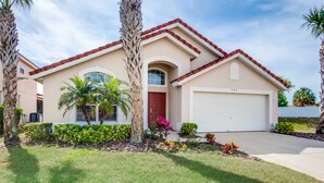 A two-story house with a red roof, a garage, and a well-maintained lawn with palm trees and colorful plants. - Aviana - Pet Friendly 4bd/3ba Pool Home - #4av242 (Davenport)