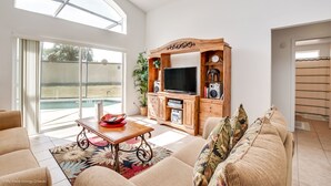 A spacious living room with a large TV, wooden entertainment unit, and a sliding glass door leading to a pool. - Aviana - Pet Friendly 4bd/3ba Pool Home - #4av242 (Davenport)