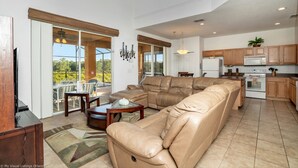 A spacious living area with a large leather sectional sofa, a dining table with chairs, and a kitchen with wooden cabinets and a microwave.