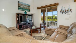 A spacious living room with leather sofas, a flat-screen TV, and a dining area with a glass door leading to a balcony.