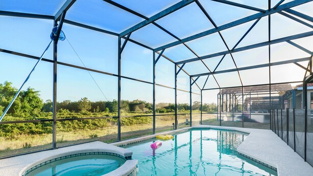 A swimming pool with a hot tub, surrounded by a glass enclosure, offering a view of the outdoors.