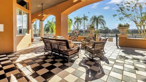 A sunlit outdoor patio with checkered flooring, wicker furniture, and ceiling fans.