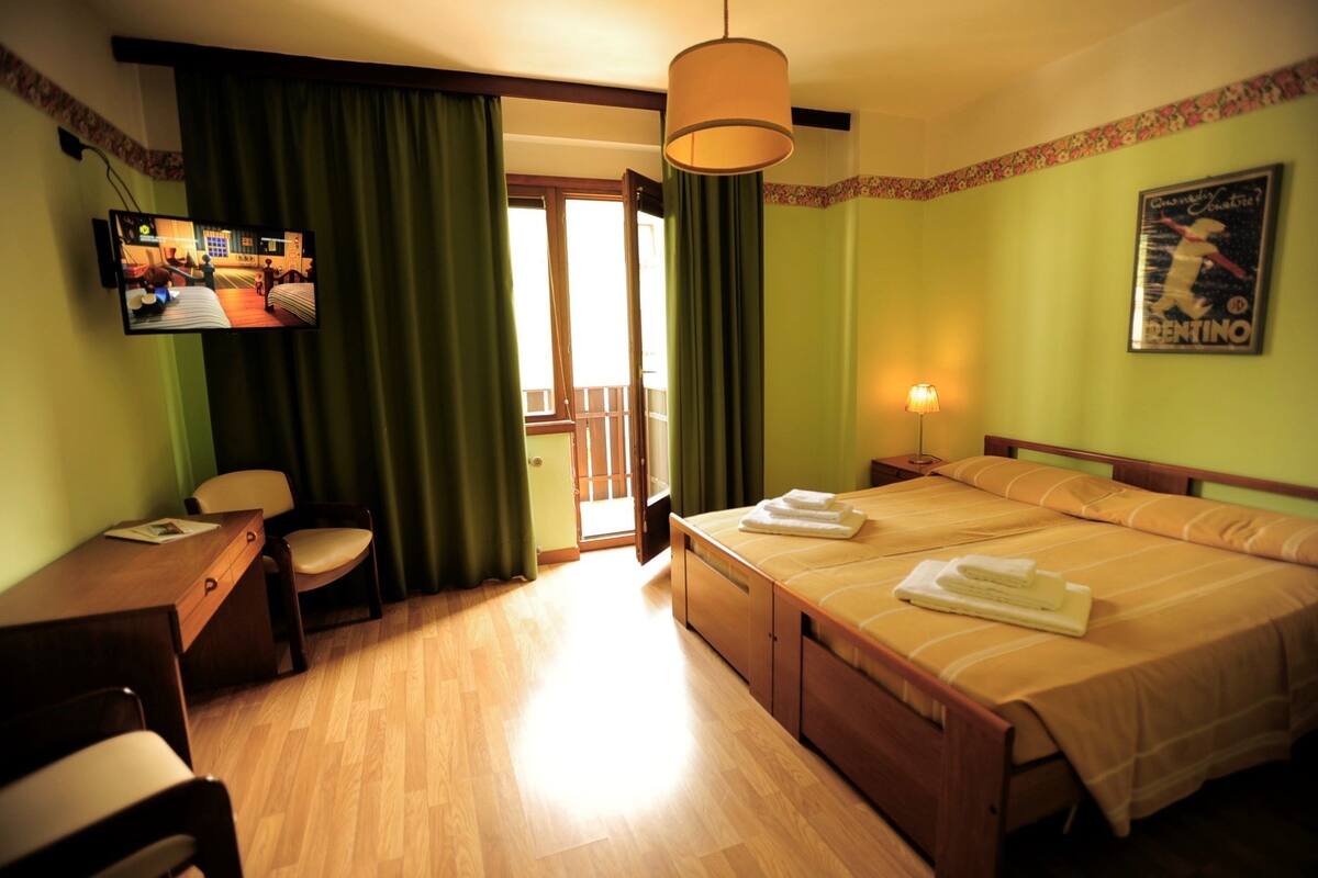 Ein Hotelzimmer mit Bett, Schreibtisch, Stuhl, Fernseher und einem Balkon.