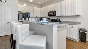 A modern kitchen with white cabinetry, a granite countertop, a built-in microwave, and a stainless steel refrigerator. - Davenport - Stunning 6bd/5ba Poolhome - #6av331 (Davenport)