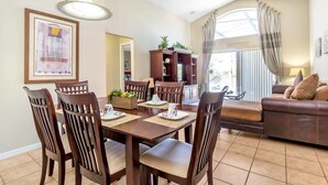 A dining area with a table set for four, surrounded by wooden chairs. There is a sofa and a cabinet in the background. - Aviana Resort - Lovely 4bd/3ba Pool Home - #4av141 (Davenport)